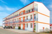 White three-story motel building with orange trim and doors to rooms on the outside, with a grey sedan parking in front of the building.