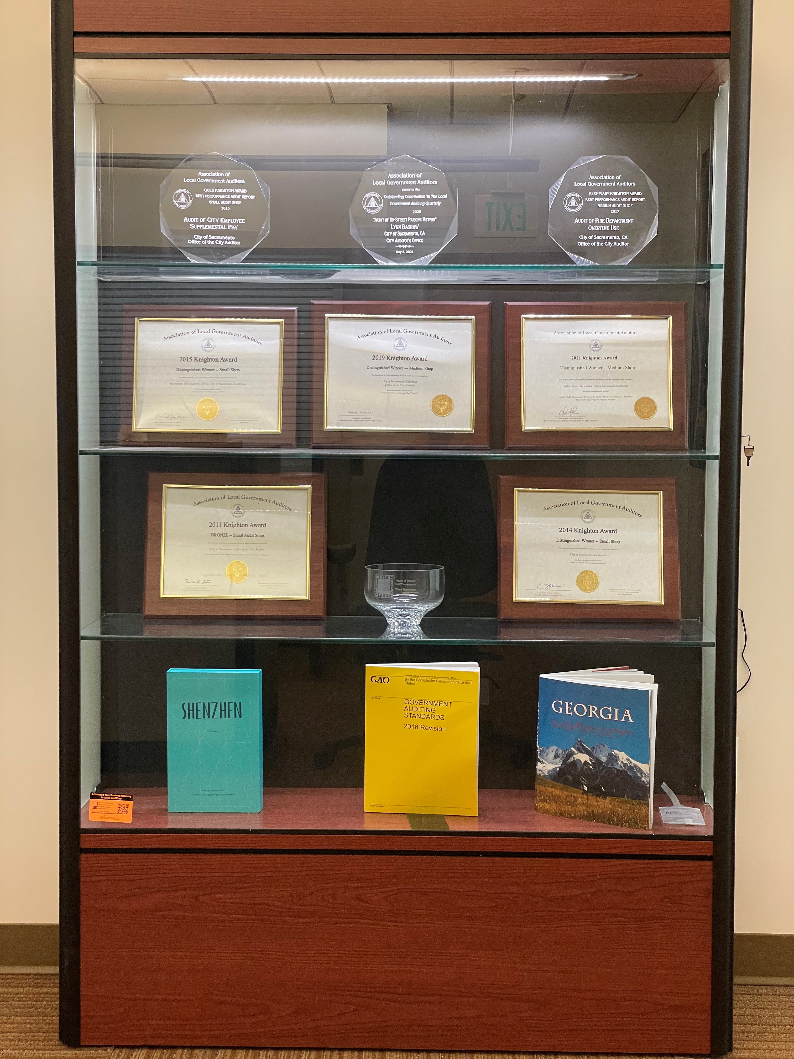 Award bookcase: top shelf three statues, second shelf three certificates, thrid shelf two certificates, bottom shelf three books