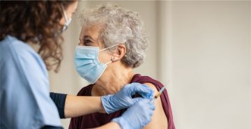 Older adult wearing mask and being vaccinated by a female nurse