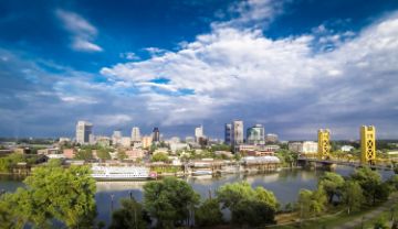 Sacramento skyline with trees closest, then river, then downtown with yellow bridge on the right