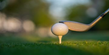 Golf ball on tee with golf club in position to hit it