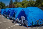 Multiple identical blue camping tents in a row on concrete with an upside down bicycle on the outside of the closest tent