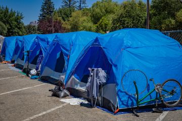 Multiple identical blue camping tents in a row on concrete with an upside down bicycle on the outside of the closest tent