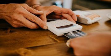 Hand making a credit card payment on a handheld device held by another person