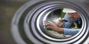 Worker inspecting the inside of a pipe with a flashlight