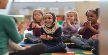 Adult leading children sitting in a group clapping