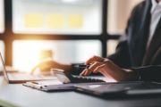 Woman in office wear working on laptop while using separate calculator with pen in hand
