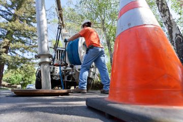 Orange safety cone with utility worker and equipment in the background