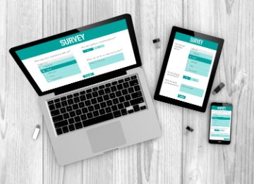 Teal and white online survey form on laptop, tablet, and phone on a light grey wooden desk