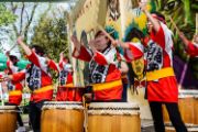 Taiko drummers in colorful costumes play larger drums with bachi (drumsticks)