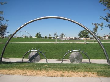 A large art piece in a park made from brushed, shiny stainless steel depicts two eyes peeking up as if from behind the hill.