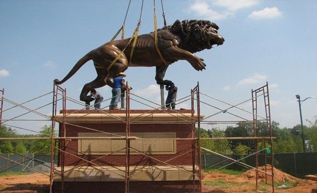 Workers setting a large bronze lion onto a pedestal.