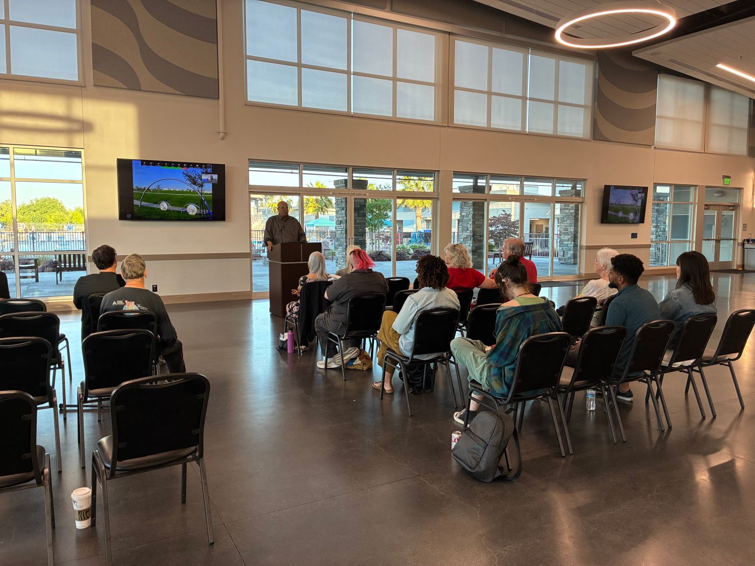 A group of adults make up an audience for a speaker. The speaker stands at a podium with a screen behind him on which are images of art.