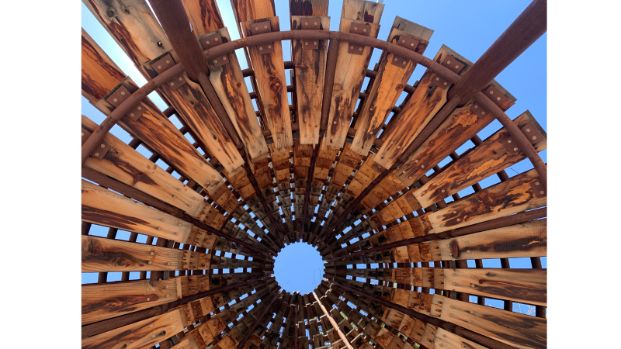 Wooden slats radiate outward in a sunburst formation. Perspective is skewed from the image but it was photographed from below loooking up through the center of the work.