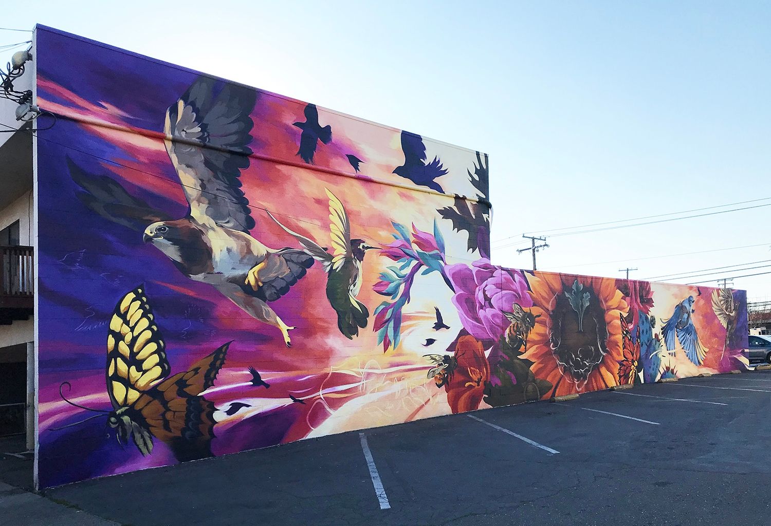 A colorful mural depicts birds swooping and insects buzzing among beautiful flowers in rich warm colors.