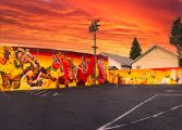 The swirling yellow, red, greens and gold of the mural depicting Ballet folklorico dancers blends seamlessly into a vivid orange sunset