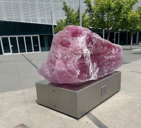 A large, opaque pink rock sits atop a stainless steel pedestal.