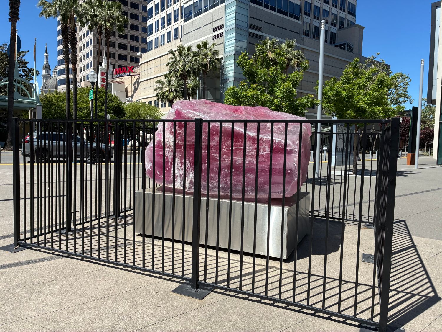 An opaque pink rock sits atop a stainless steel pedestal, enclosed by a black fence.
