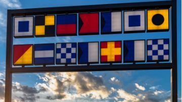 Geometric Shapes in blue, red, yellow, black and white are placed in a black frame against a blue sky with striling clouds.