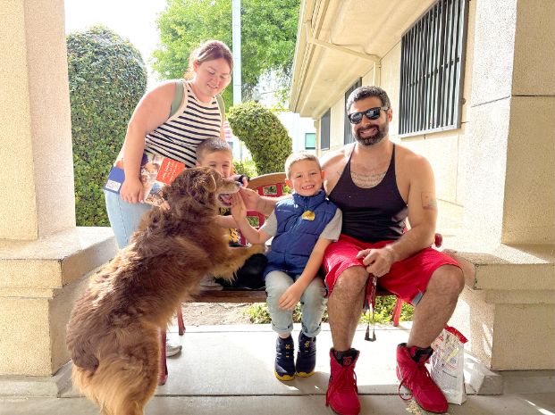 Dog named Finn climbing up with his new family sitting on a bench in front of the animal shelter