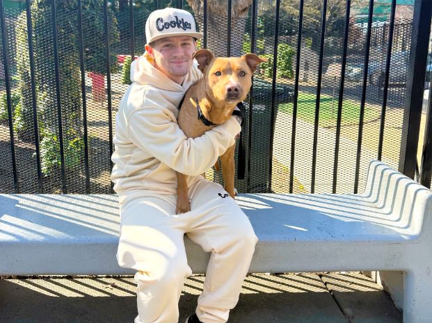 Ziggy, who is a male tan Pit Bull, sitting on a bench with his new adopter in front of the play yard