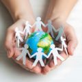 two hands cupped holding a miniature globe and a paper cut-out of people connected together