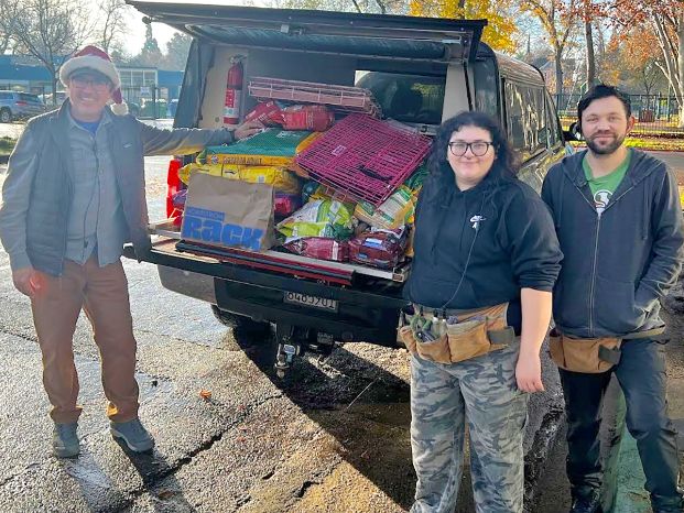 three people standing by the back of a truck filled with donated pet items