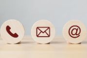 photo of three wooden round block with a picture of a phone, envelope and an @ sign on a light wooden base.