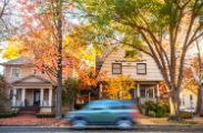 Photo of two houses in a neighborhood with a car driving past.