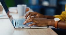 Close up shot of African American female hands typing on laptop while sitting at office desk indoors