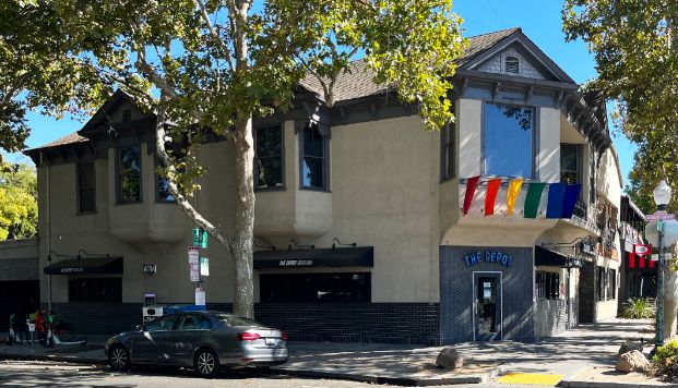 Corner 2-story building withrainbow flags hung from the second floor. 