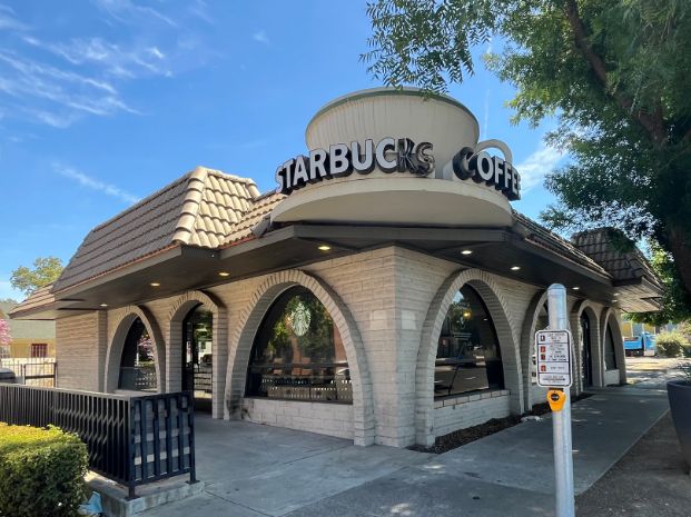 Corner building with arched windows and a large coffee cup on the roof with "Starbucks Coffee" written on it. 