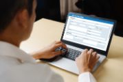 An over the shoulder view of a man working on a laptop.