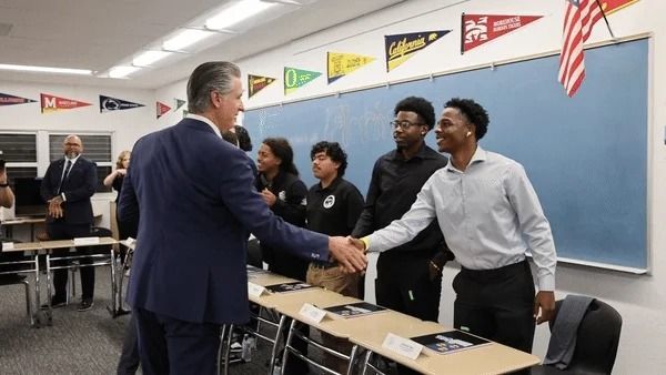 Young man in classroom shakes Governor Newsom's hand while several other young men in line wait to shake his hand