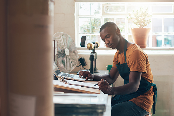 Man sitting at desk looking over documents with window and sunlight behind him.