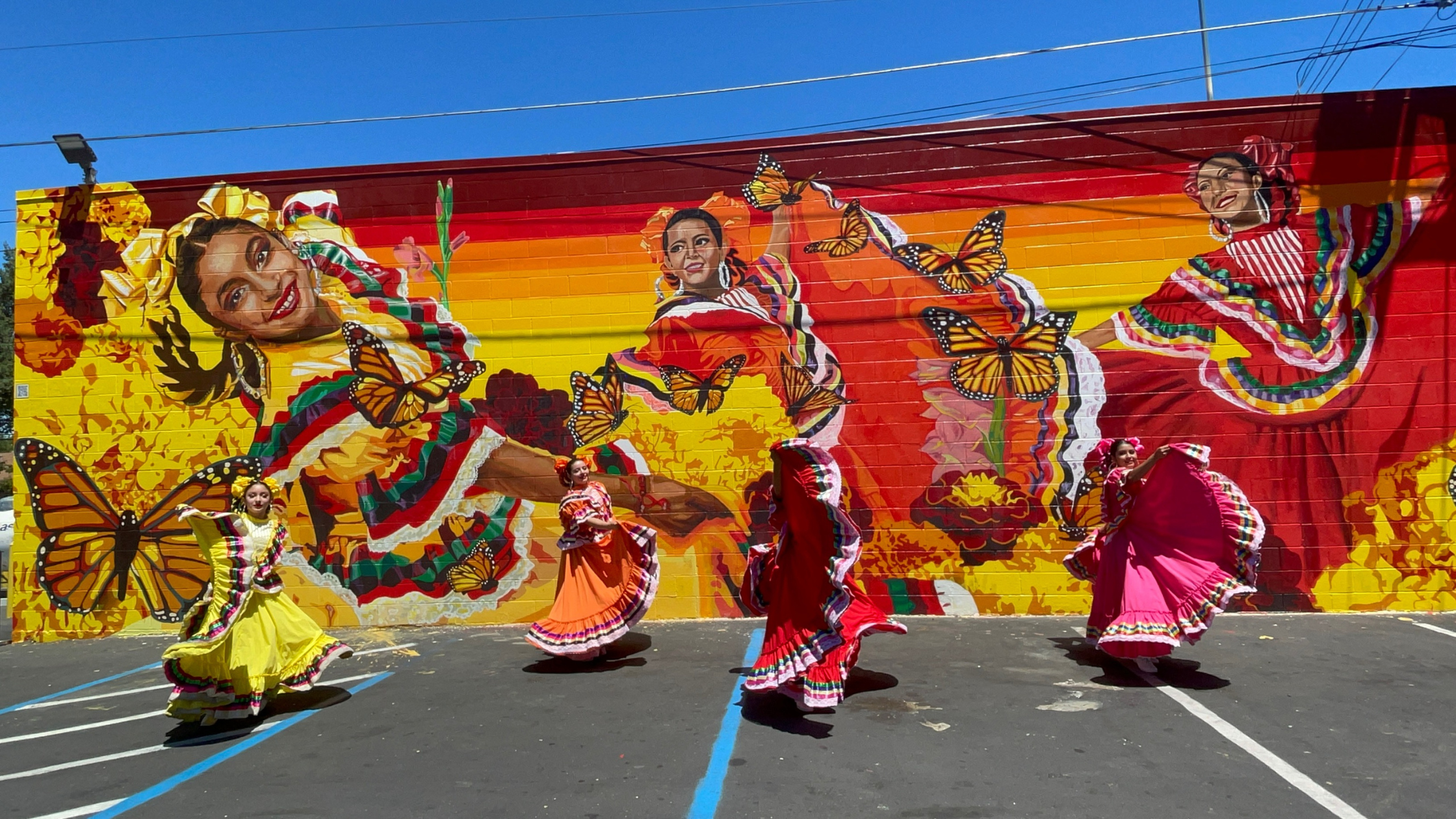 People dancing in festive colorful dresses infront of art mural