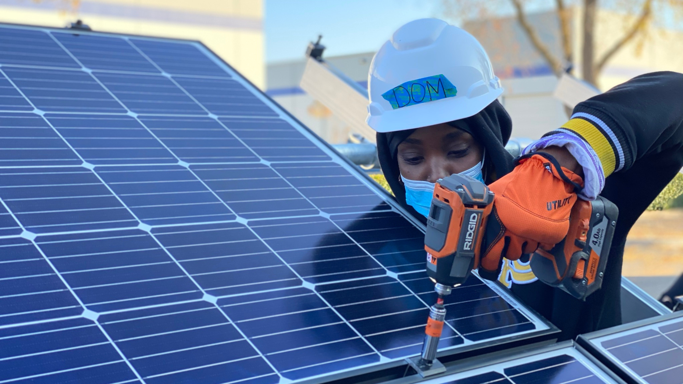 A worker installs solar panels using a drill. 