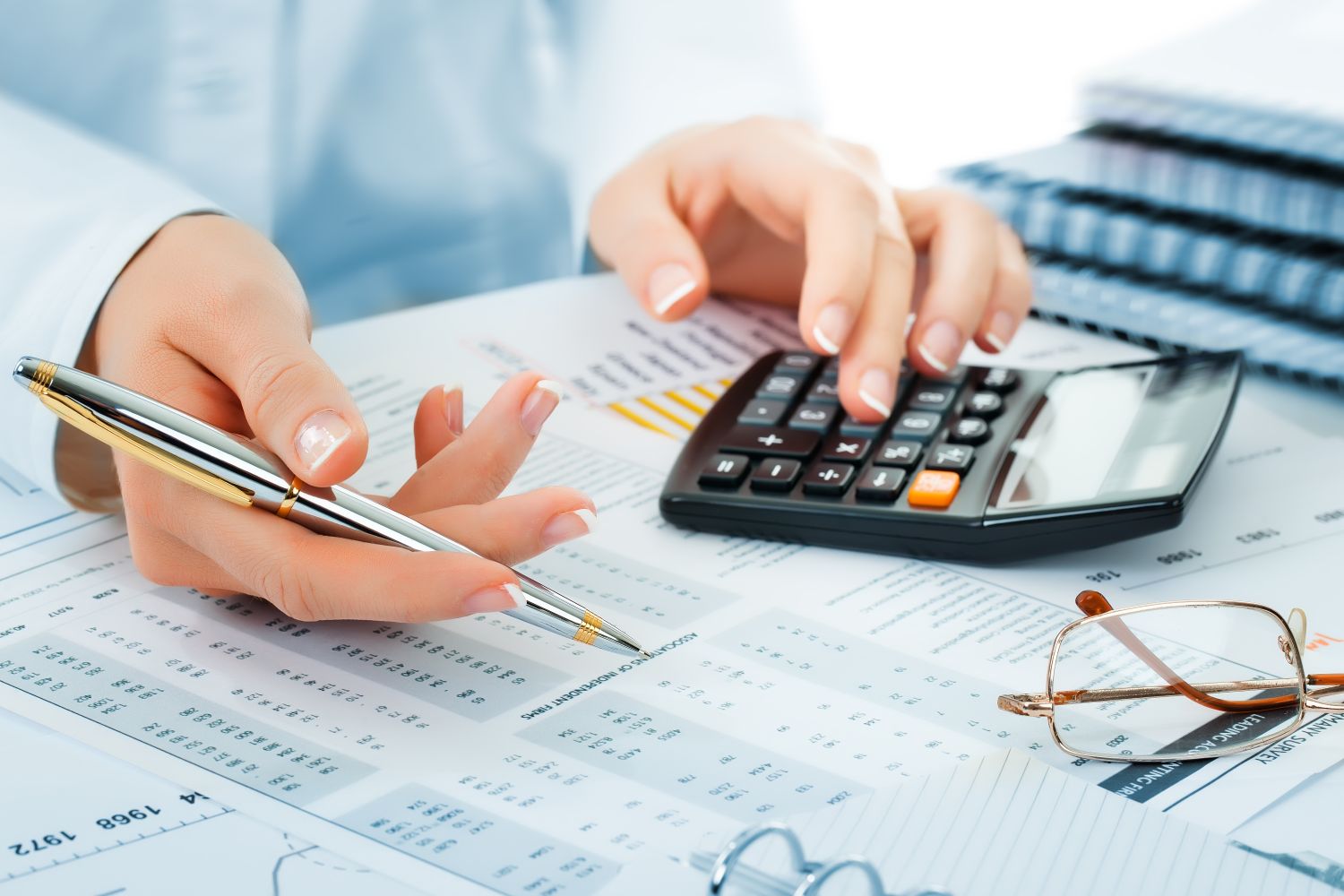 hands holding a pen and typing on a calculator with numbers on a paper