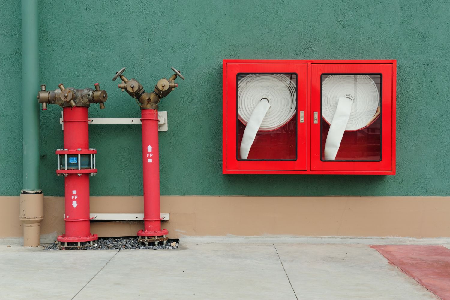 Image of two fire hoses enclosed in red, square glass cases and two stand pipes to the left