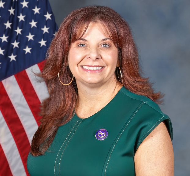 Photo of fire admin manager Anne Iturraran in a sleeveless green dress with a U.S. flag and gray background.