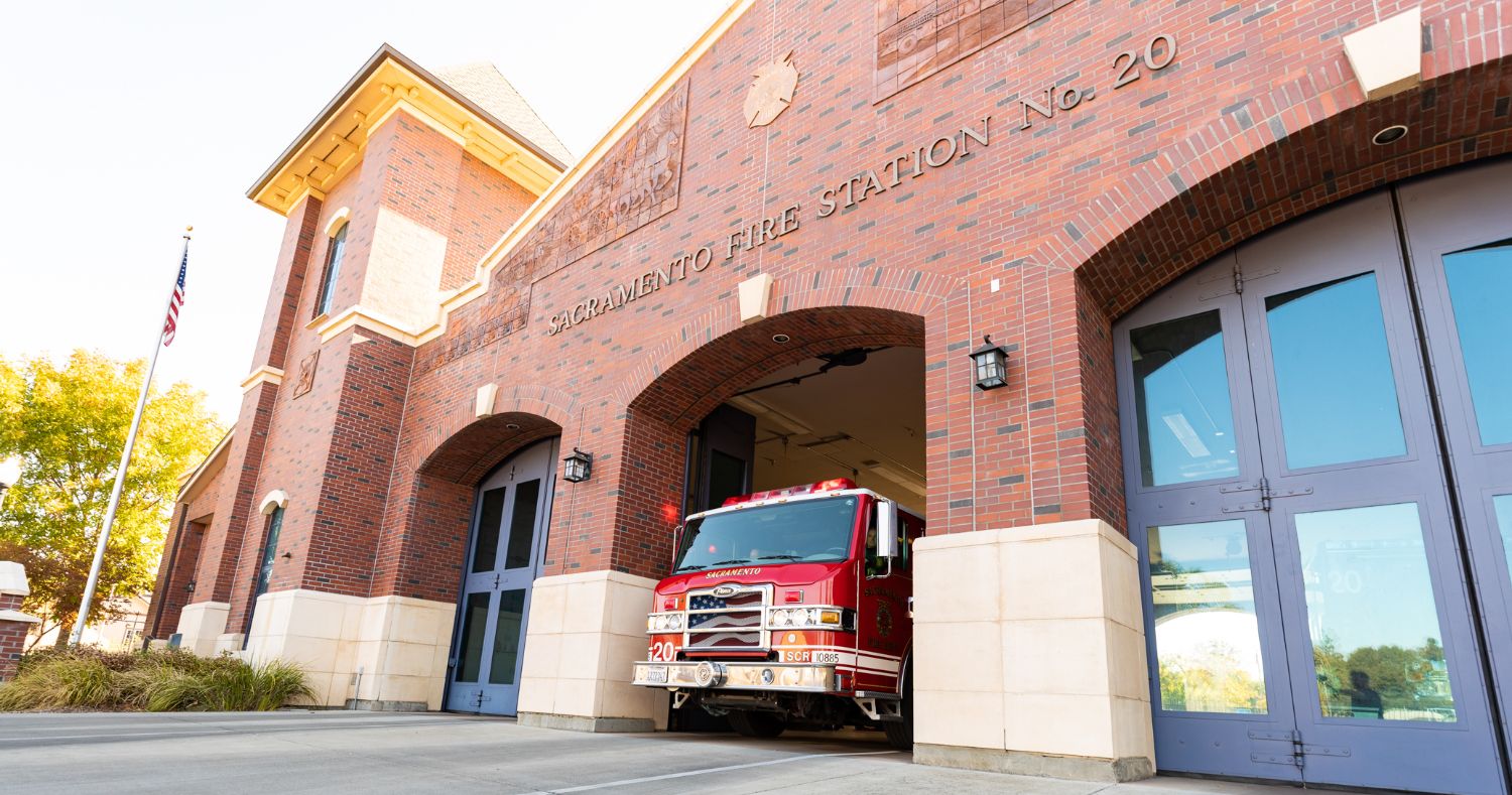 A side photo of Station 20, a brick building with glass garage doors, and engine coming out of one of the doors. 
