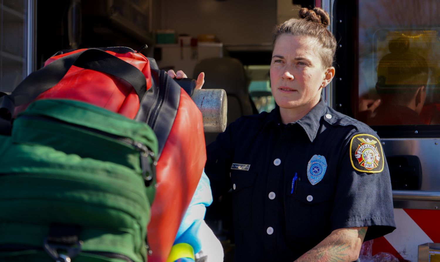 Sacramento paramedic pushing a gurney with a red and green bag. Behind her is an ambulance.