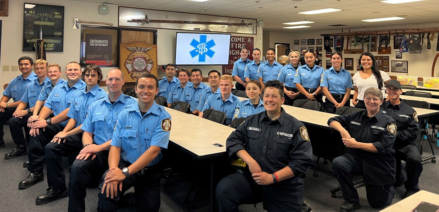Group photo of EMS trainees in light blue and staff in navy, some standing, some sitting