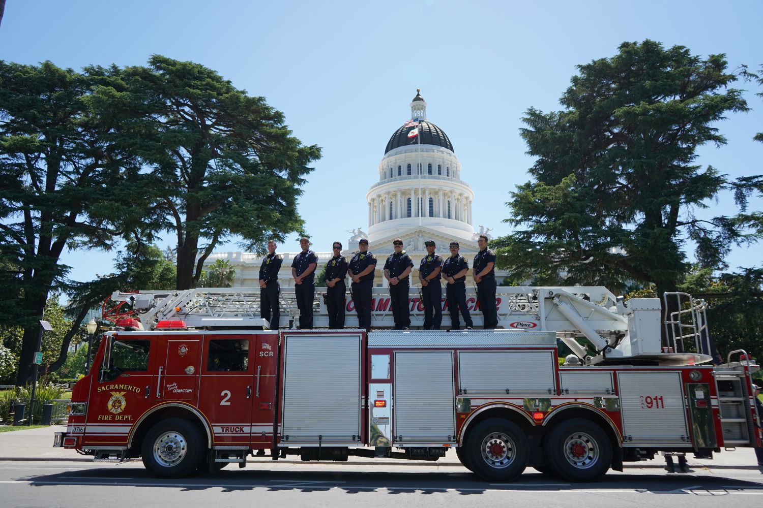 FIRE TRUCK 2 WITH FIREFIGHTERS STANDING ON TOP OF THE TRUCK IN FRONT OF THE CAPITOL