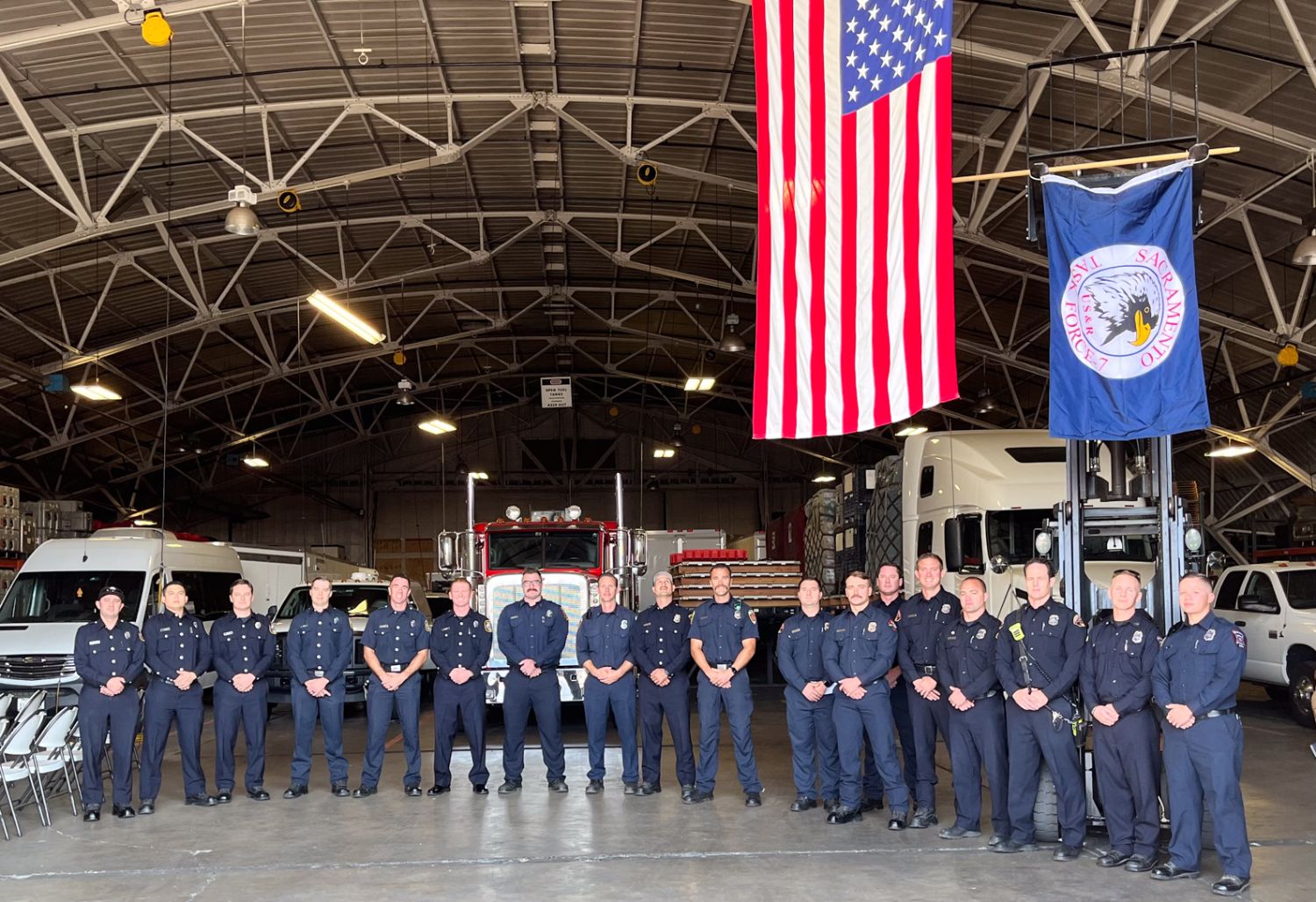 a group of firefighters standing in line with two flags over them.