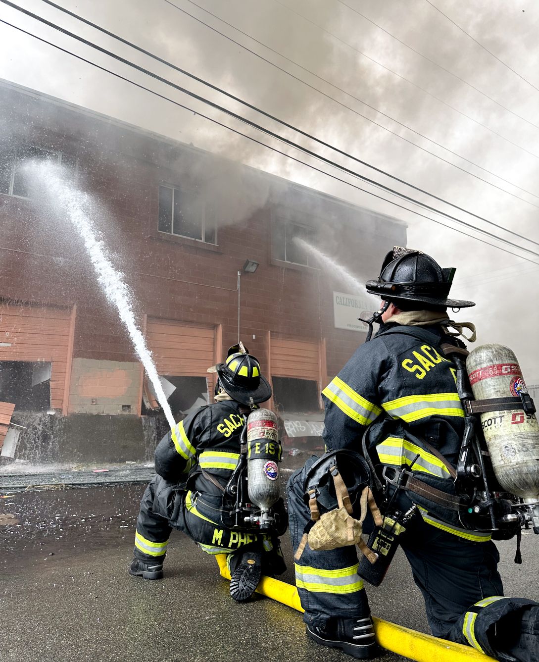 two firefighters fighting a structure fire on their knee holding a water hose.