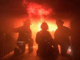 three firefighters on their knees during a training exercise looking toward the flames of a fire.