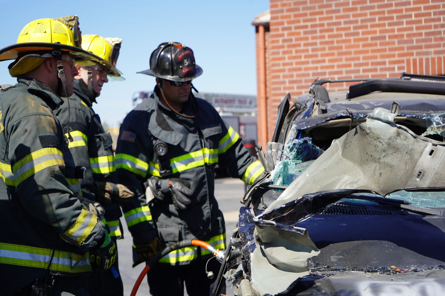 three firefighters looking at a wrecked vehicle in a training scenario 