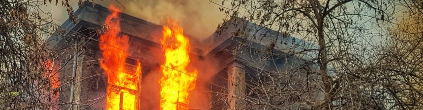 A burning house with trees in front of it.