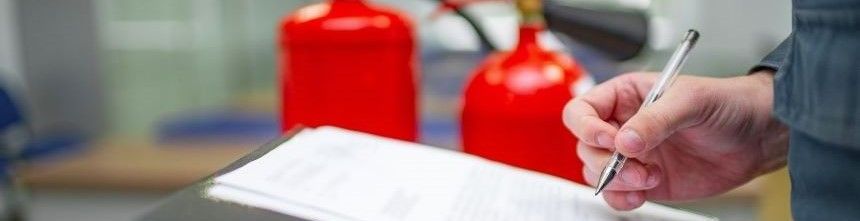Fire Prevention officer inspecting a fire extinguisher and recording the information on a clipboard form.. Red fire extinguisthers in the background.
